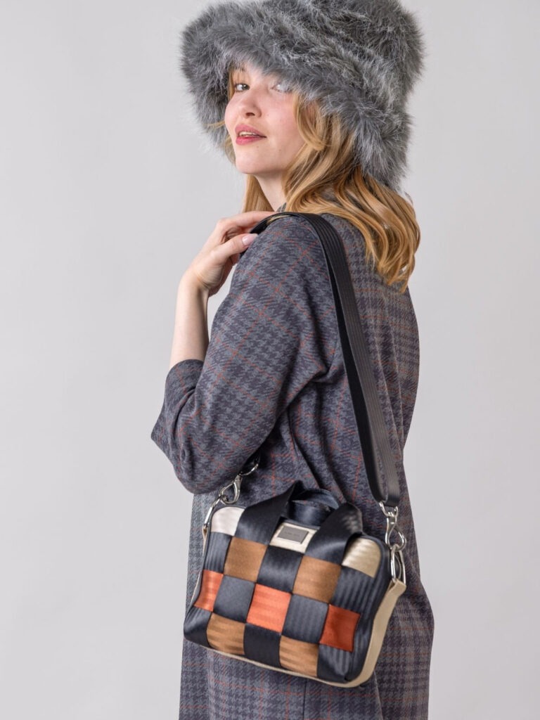 Woman with a large hat is looking at the camera and holding a multicoloured HILLA bag on he shoulder