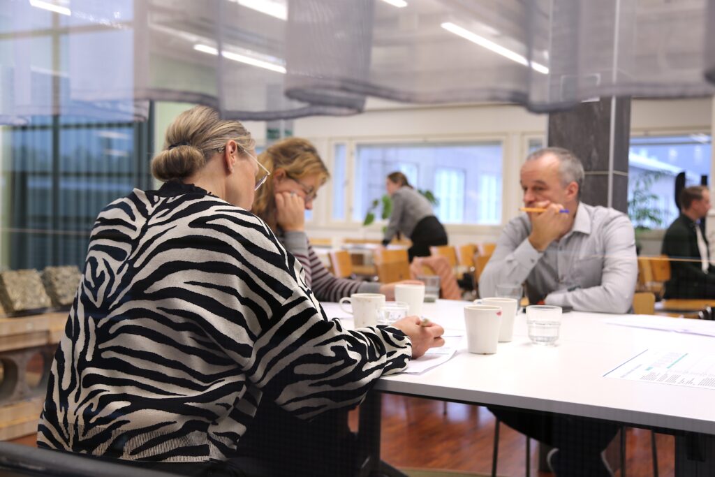 Kolme ihmistä työskentelee pöydän ympärillä ja täyttää lomakkeita.